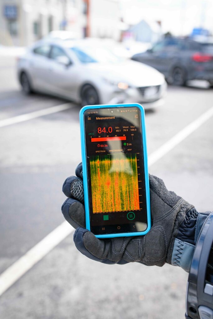 Smartphone showing decibel readings and noise spectrum while measuring traffic noise outdoors